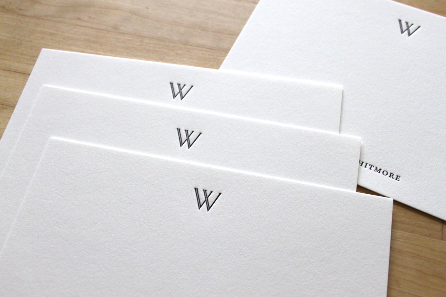 Close-up of letterpress impression on cotton paper notecard, double-stroke serif initial W, deep ink impression, handcrafted professional stationery