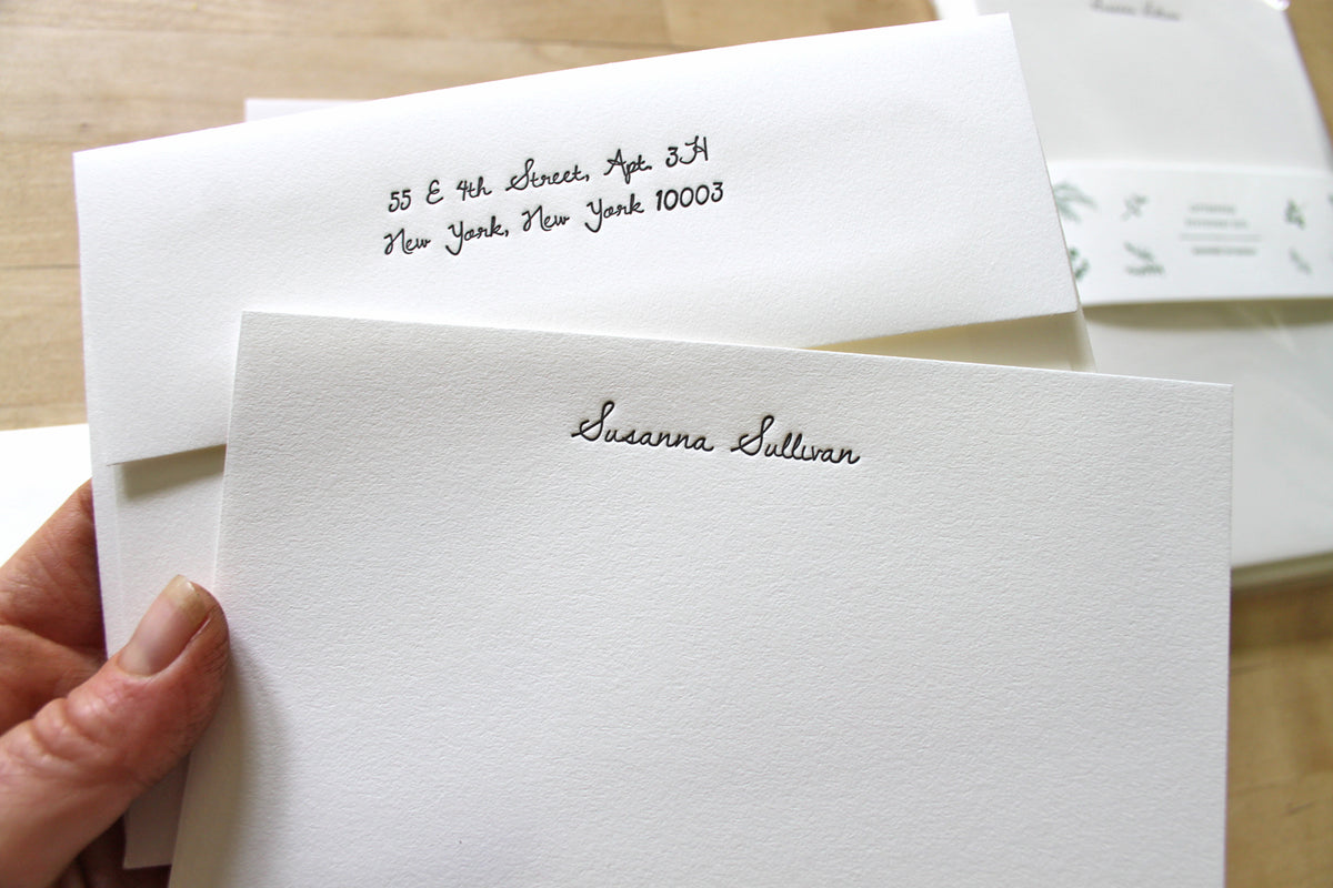 Letterpress stationery shown in handwriting font option, with hand holding letter sheet and matching cursive-addressed envelope