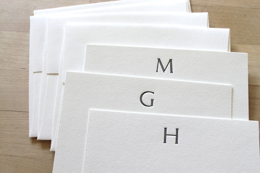 Stack of custom letterpress notecards with initials 'M', 'G', and 'H' on a wooden surface