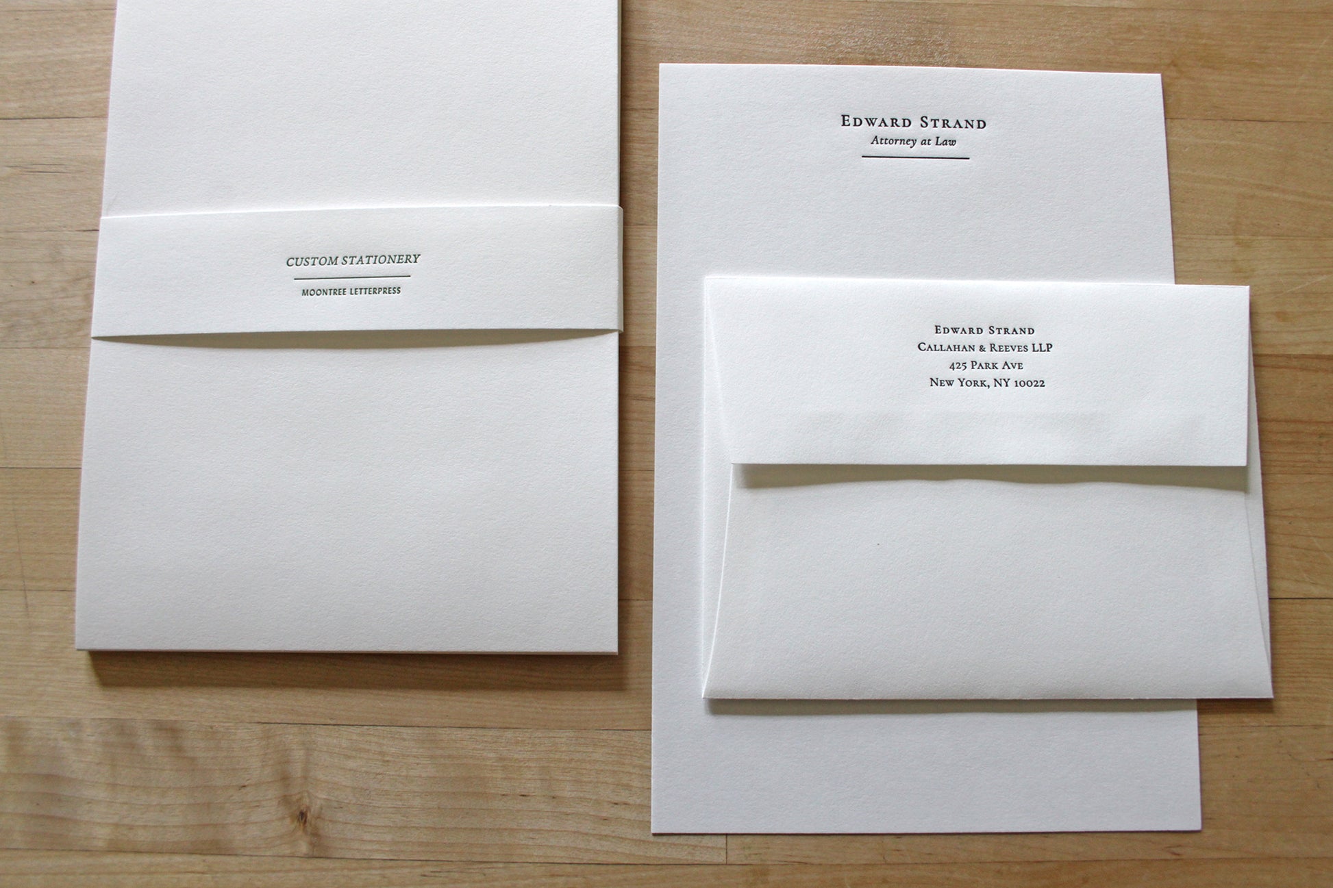 Letterpress stationery set including a letter sheet, and a matching envelope with a printed address, arranged on a light wood background.