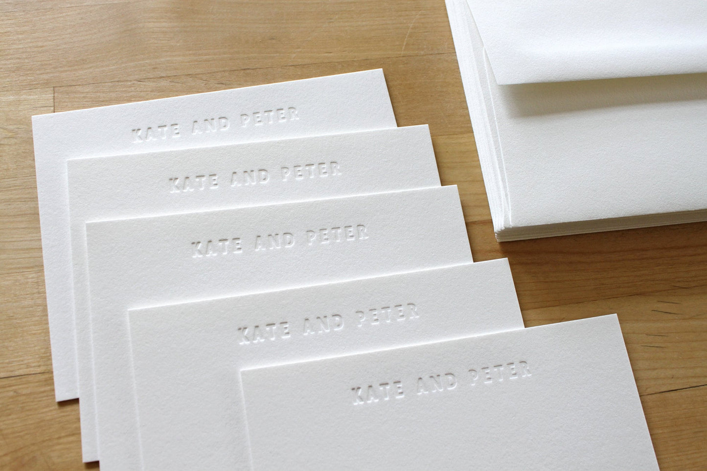 Fan of blind embossed bold type personalized letterpress notecards on wooden surface