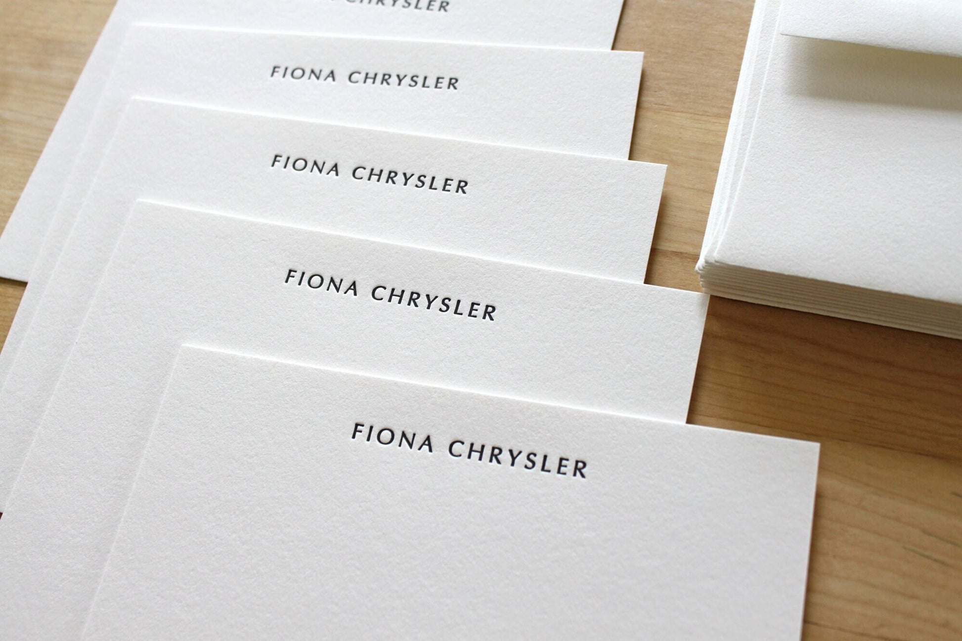 Stack of Optima style letterpress notecards with matching envelope on wooden surface