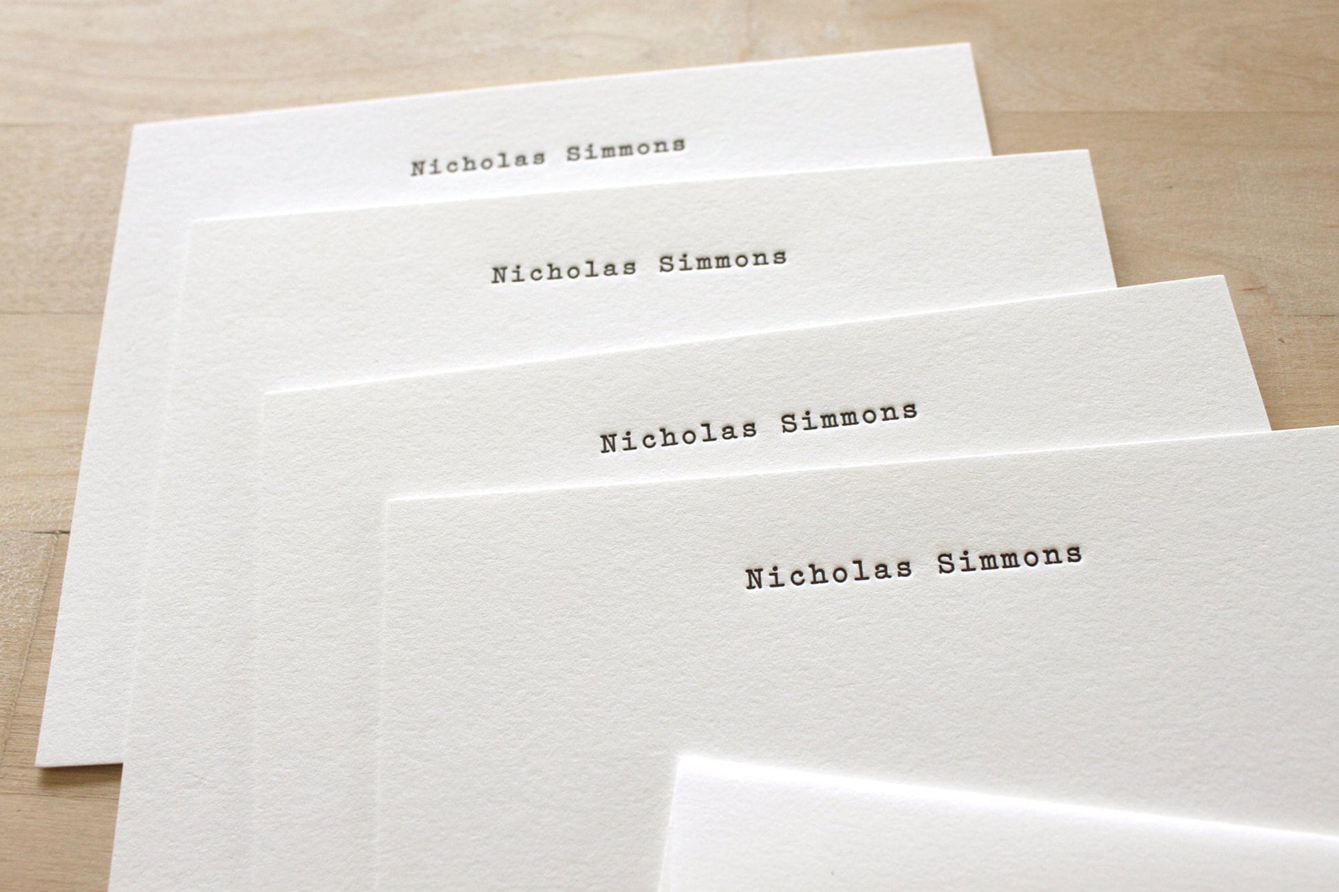 Stack of typewriter style letterpress statiomery with name fanned on wooden surface