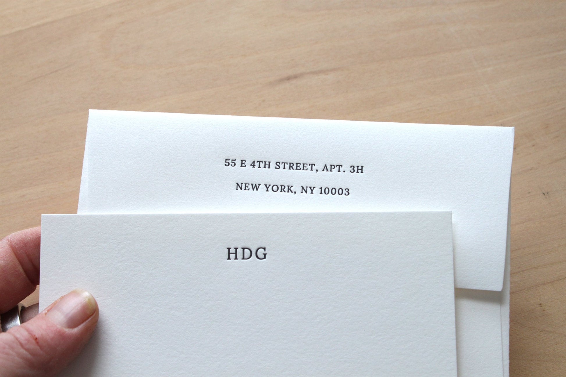 Hand holding small initials letterpress stationery with monogram and return address