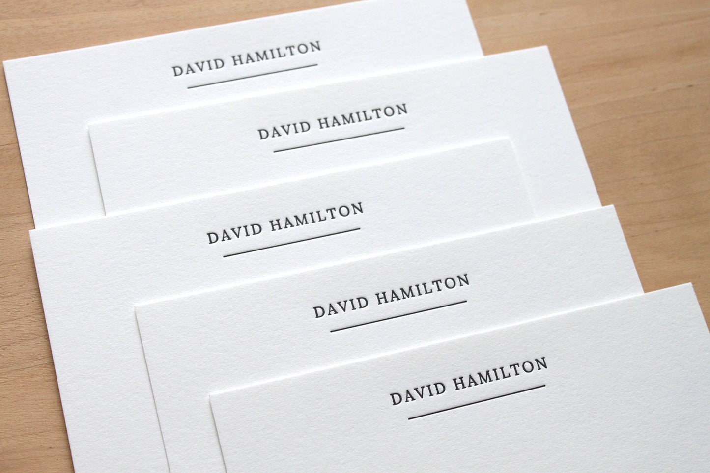 Stack of stately underlined personalized letterpress notecards fanned on wooden surface