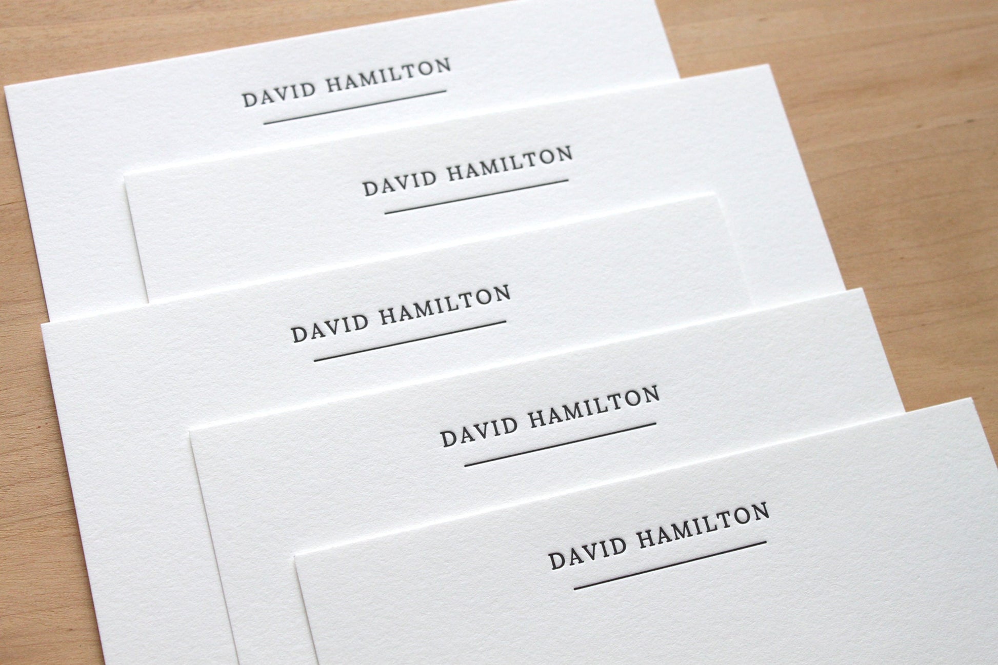 Stack of stately underlined personalized letterpress notecards fanned on wooden surface